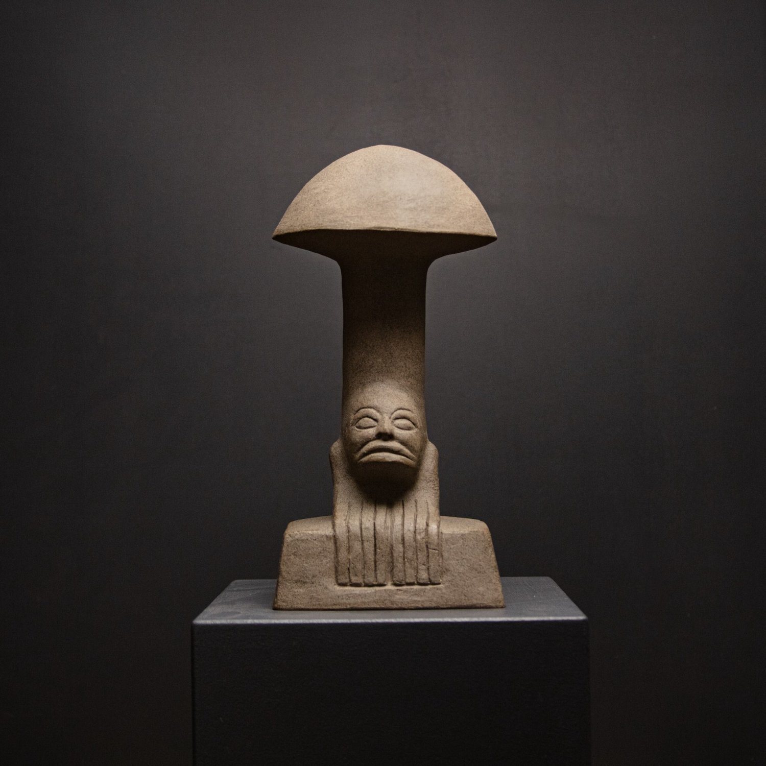 Stone mushroom sculpture with a carved face, on a dark plinth